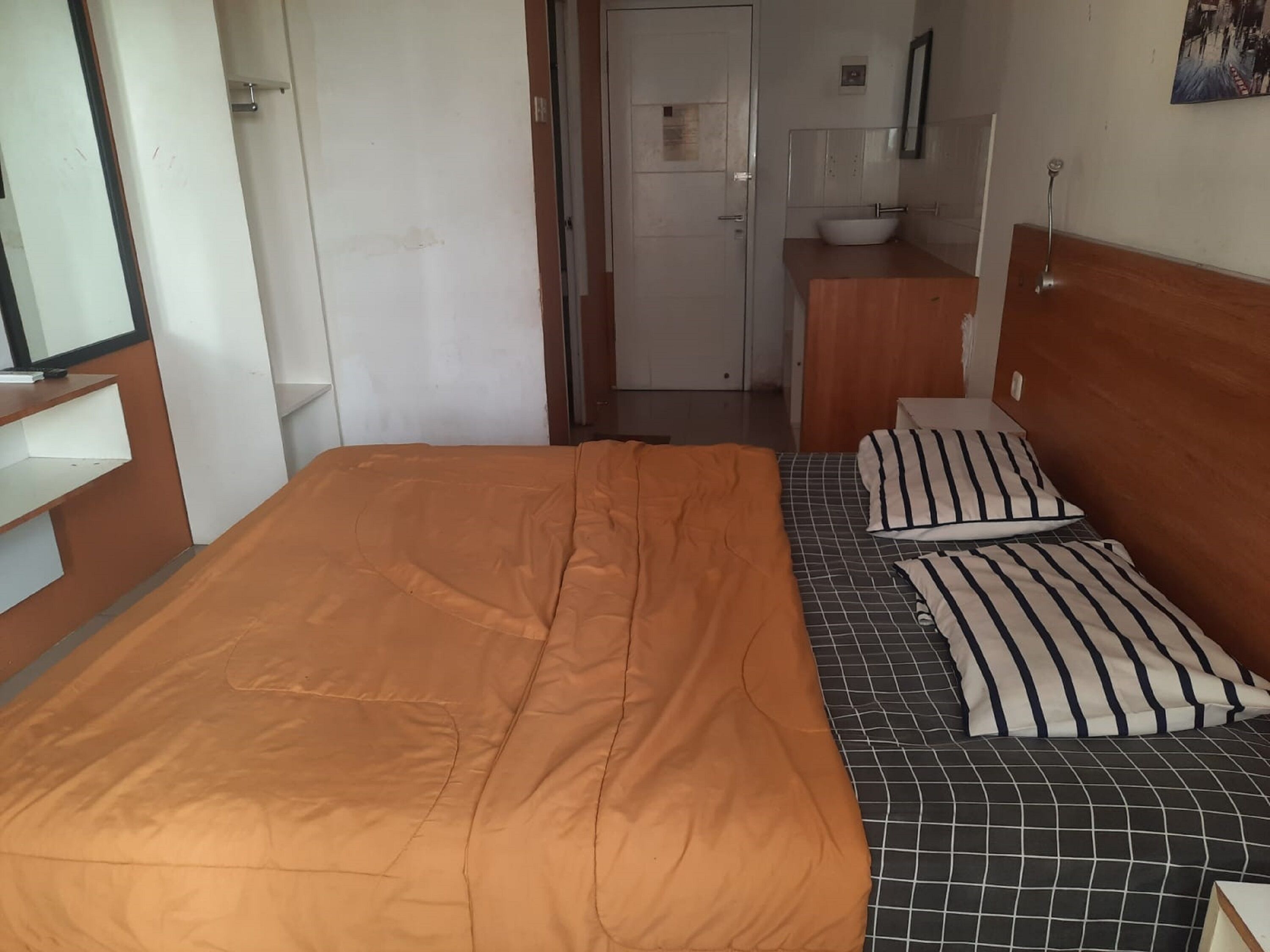 Ein Schlafzimmer mit Bett, Nachttisch, Spiegel und einem durchgehenden Türbogen einsehbarem Badezimmer.