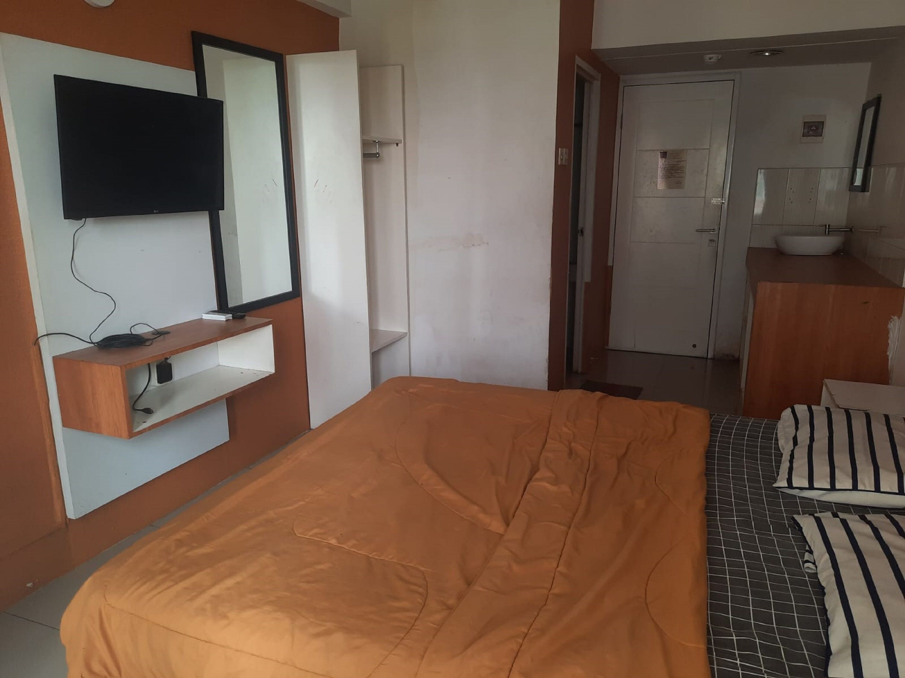 Habitación de hotel con cama, televisor montado en la pared, cómoda de madera y baño visible a través de una puerta abierta.