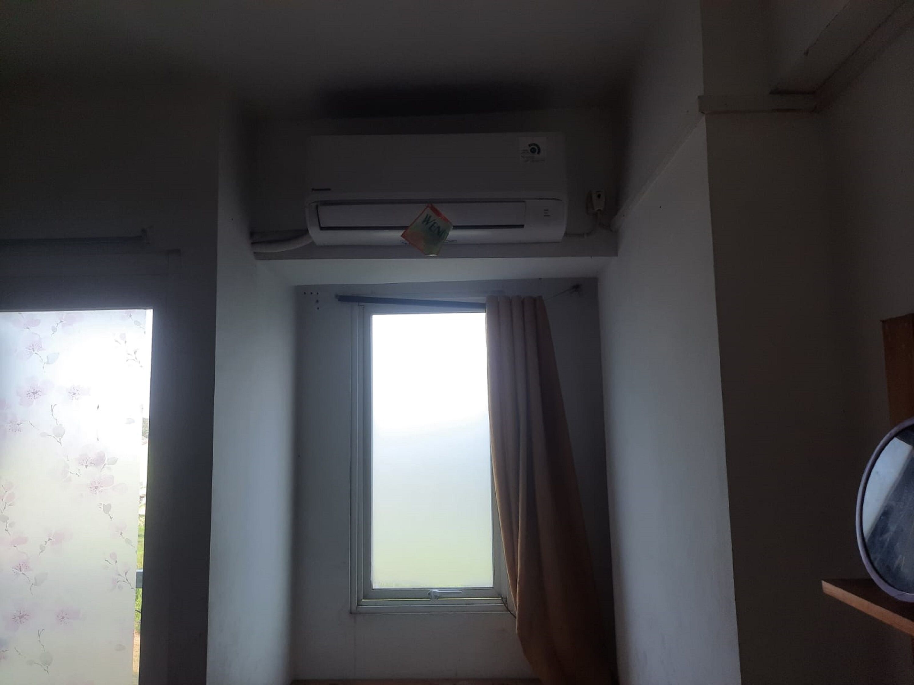 A room with a window, a door with floral curtains, and an air conditioning unit on the wall.