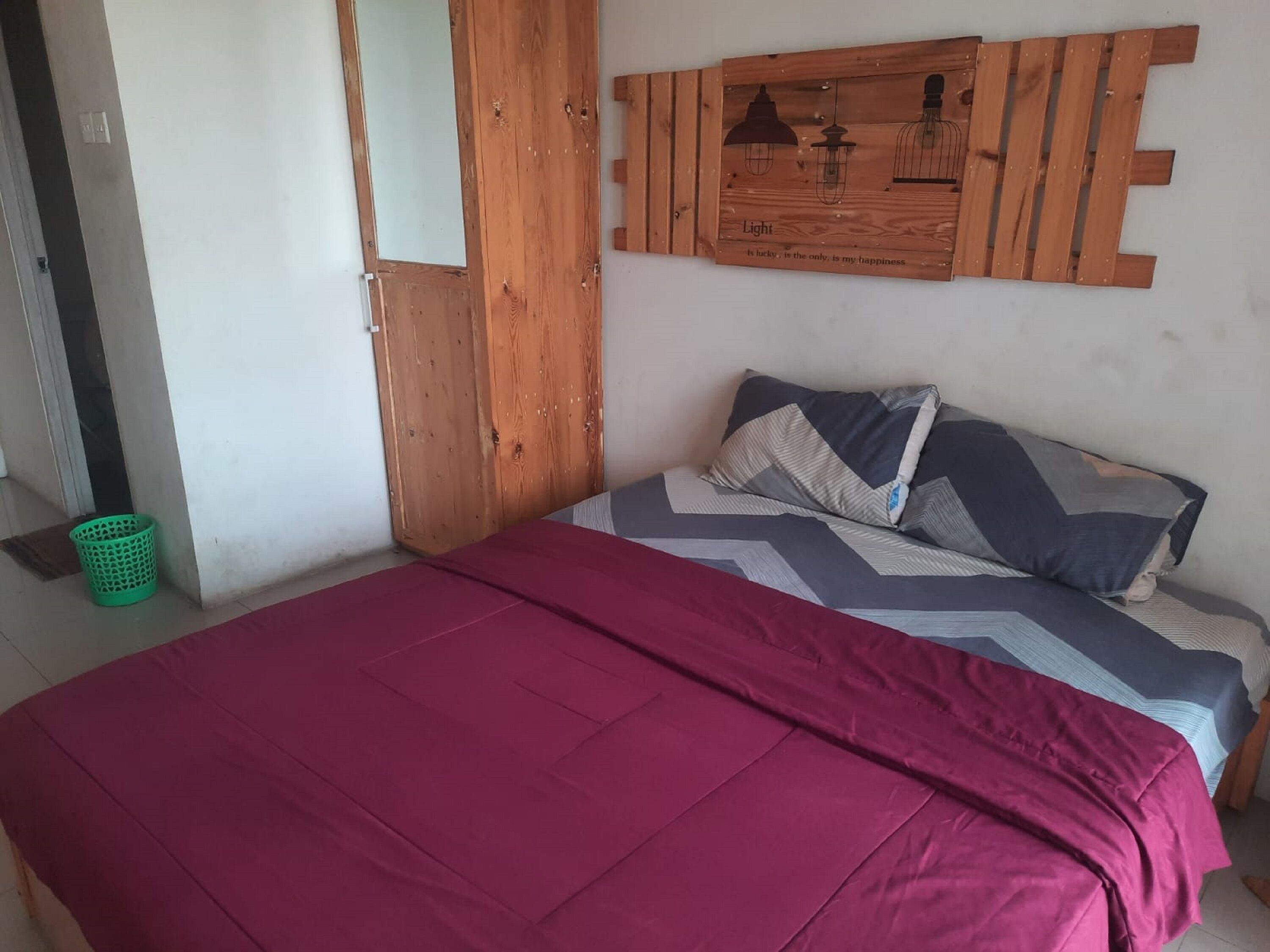 A bedroom with a bed, a wooden headboard, a green basket, and a wall-mounted light fixture.