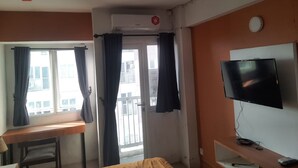 A hotel room with a bed, a desk, a TV, and a balcony with curtains. - OYO Life 93140 Apartment Grand Sentraland By Fahri (Karawang)