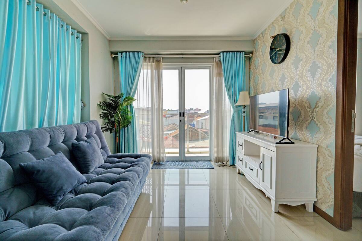Een woonkamer met een grijze bank, een televisie op een witte kast, en uitzicht door een glazen deur.