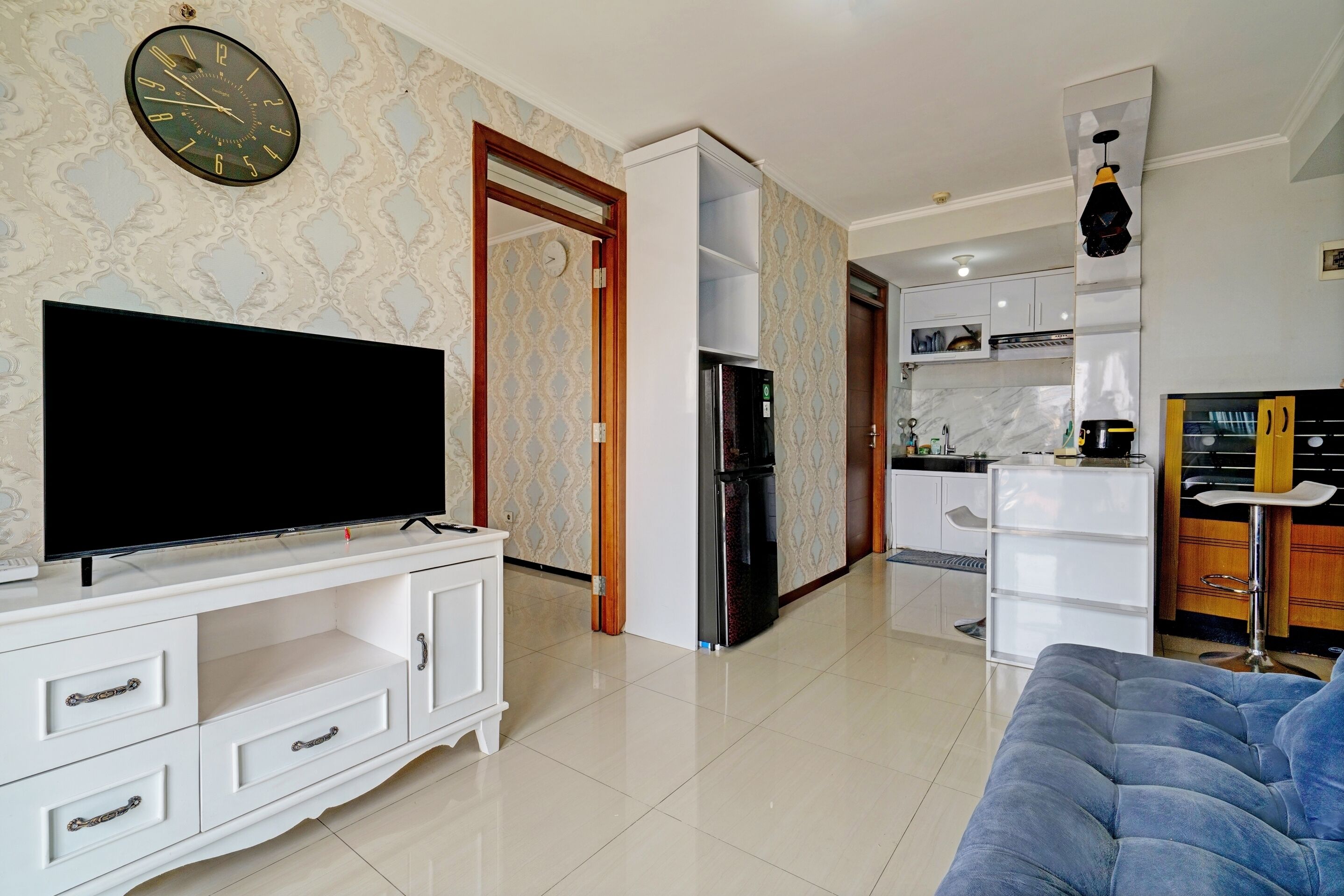 Uma sala de estar moderna com televisão de tela plana, um sofá e uma área de cozinha com armários e geladeira.