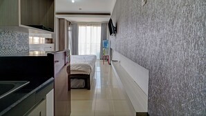 Ein Hotelzimmer mit einem Bett, einem an der Wand montierten Fernseher, einem Wasserspender und einer Küchenzeile mit Spüle und Schränken.