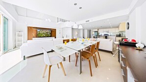 Una cocina moderna con armarios blancos, un comedor con mesa y sillas blancas, y un amplio ventanal que proporciona luz natural.