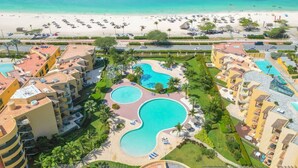 Un resort con dos piscinas grandes, una playa y un estacionamiento.