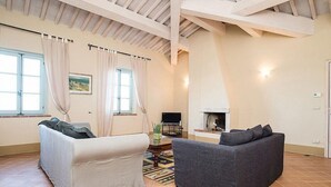 A spacious living room with a high ceiling, two sofas, a fireplace, and a television. - Casa Dracena A: A welcoming apartment situated in the heart of the Tuscan countryside, with Free WI-FI. (Trequanda)