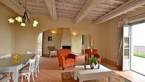 Un vaste salon doté d’une cheminée, un coin repas avec une table et des chaises, et une grande fenêtre offrant une vue sur l’extérieur.