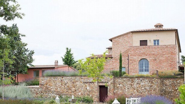 A stone building with a garden in front, featuring a stone wall, flower beds, and a small white fence.