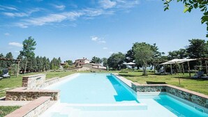 A rectangular swimming pool with stone steps leading into it, surrounded by a grassy area and trees.
