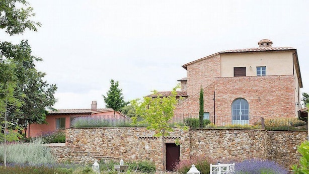 Un bâtiment en pierre avec un jardin à l’avant, comprenant un mur en pierre, des parterres de fleurs et une petite clôture blanche.