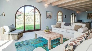 A spacious living room with a white sofa, a wicker chair, and a coffee table. Large arched windows provide a view of the outdoors.