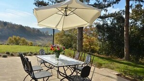 Eine Terrasse im Freien mit Tisch, Stühlen, einem großen Sonnenschirm und einem Blumenstrauß.