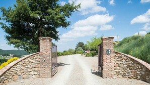 Un chemin de campagne mène à une porte en pierre, flanquée d’un mur de briques d’un côté et d’un arbre de l’autre.