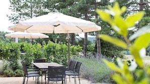Eine Terrasse im Freien mit Tisch und Stühlen, umgeben von Grünpflanzen und Bäumen.