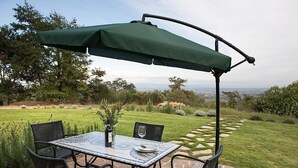 Mesa de pátio com quatro cadeiras, um guarda-sol verde e um vaso com planta.