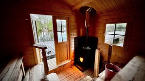 A cozy cabin with a wood-burning stove, wooden floors, and large windows offering views of a forested area.