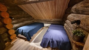 A log cabin room with two beds, a small rug, a plant, and a wall-mounted light.