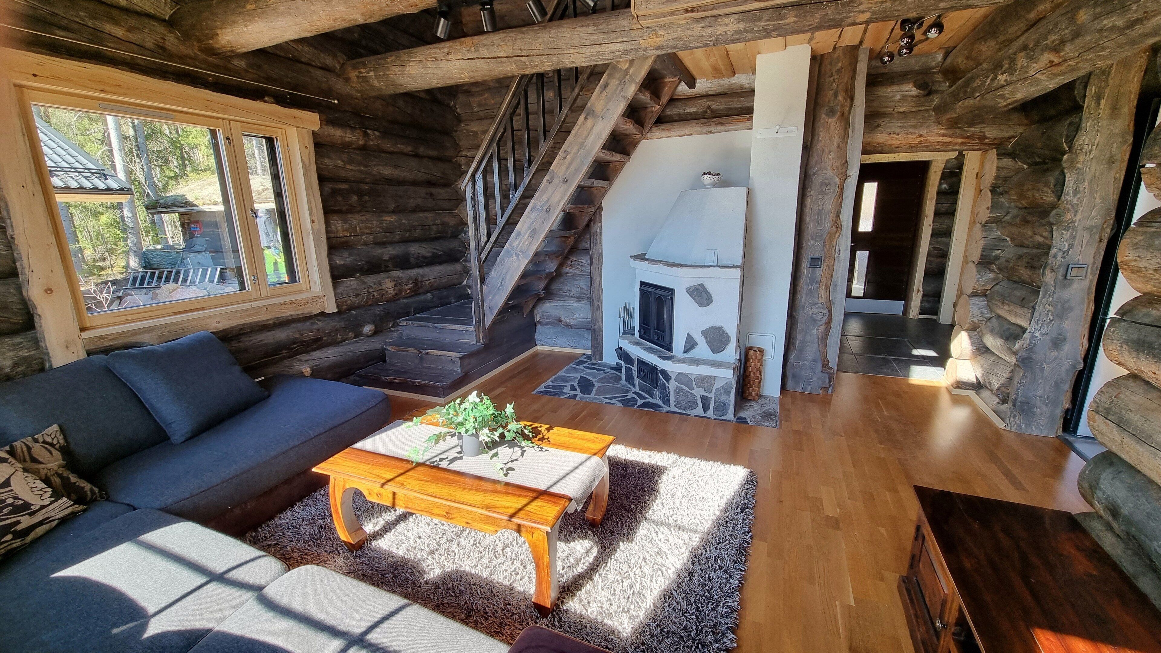 Een blokhutinterieur met een bank, salontafel, open haard en een trap naar een hoger niveau.
