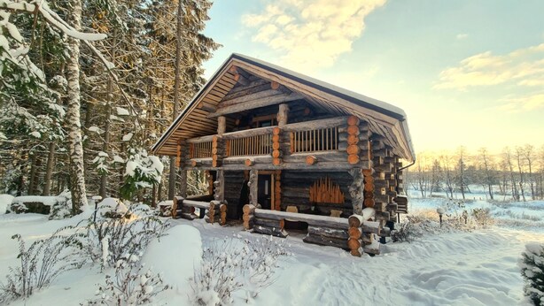 A log cabin with a balcony, surrounded by snow-covered trees and a snowy landscape.