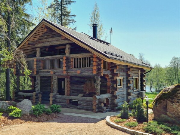 A log cabin with a balcony, surrounded by a forest.