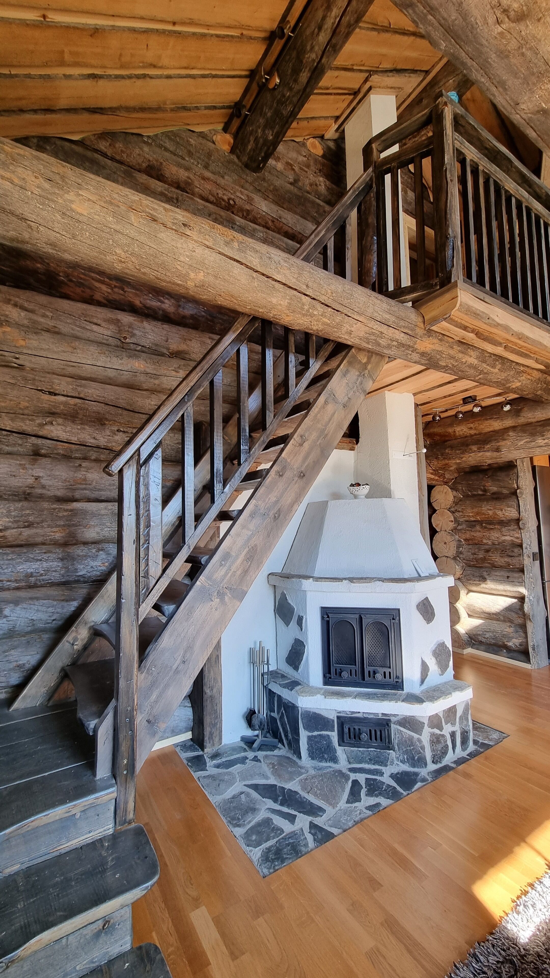 A rustic cabin interior with a stone fireplace, wooden staircase, and log walls.