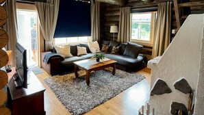 A log cabin interior with a wooden ceiling, two sofas, a coffee table, and a fireplace.
