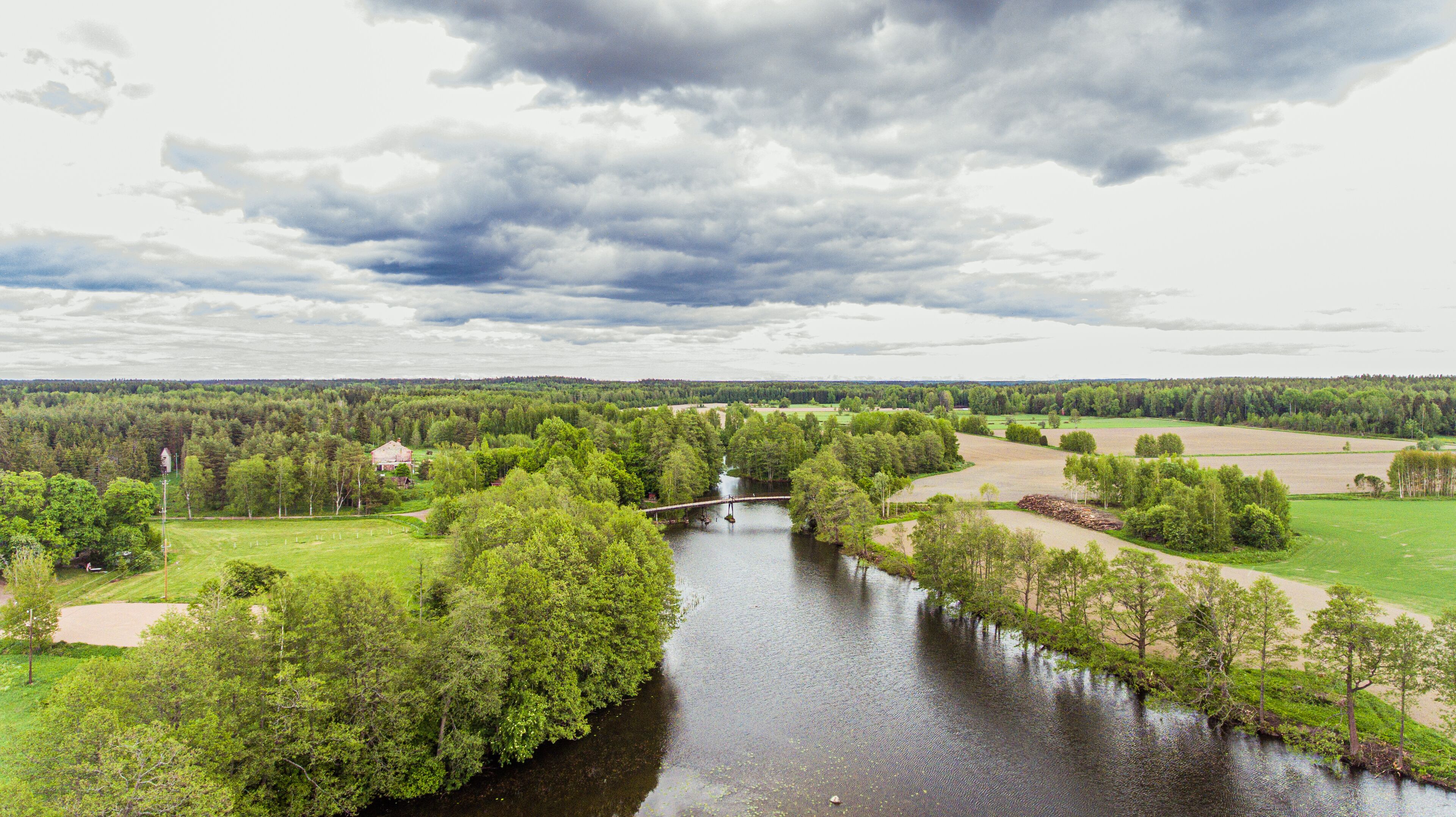 Un río con un puente, rodeado de vegetación exuberante y campos.