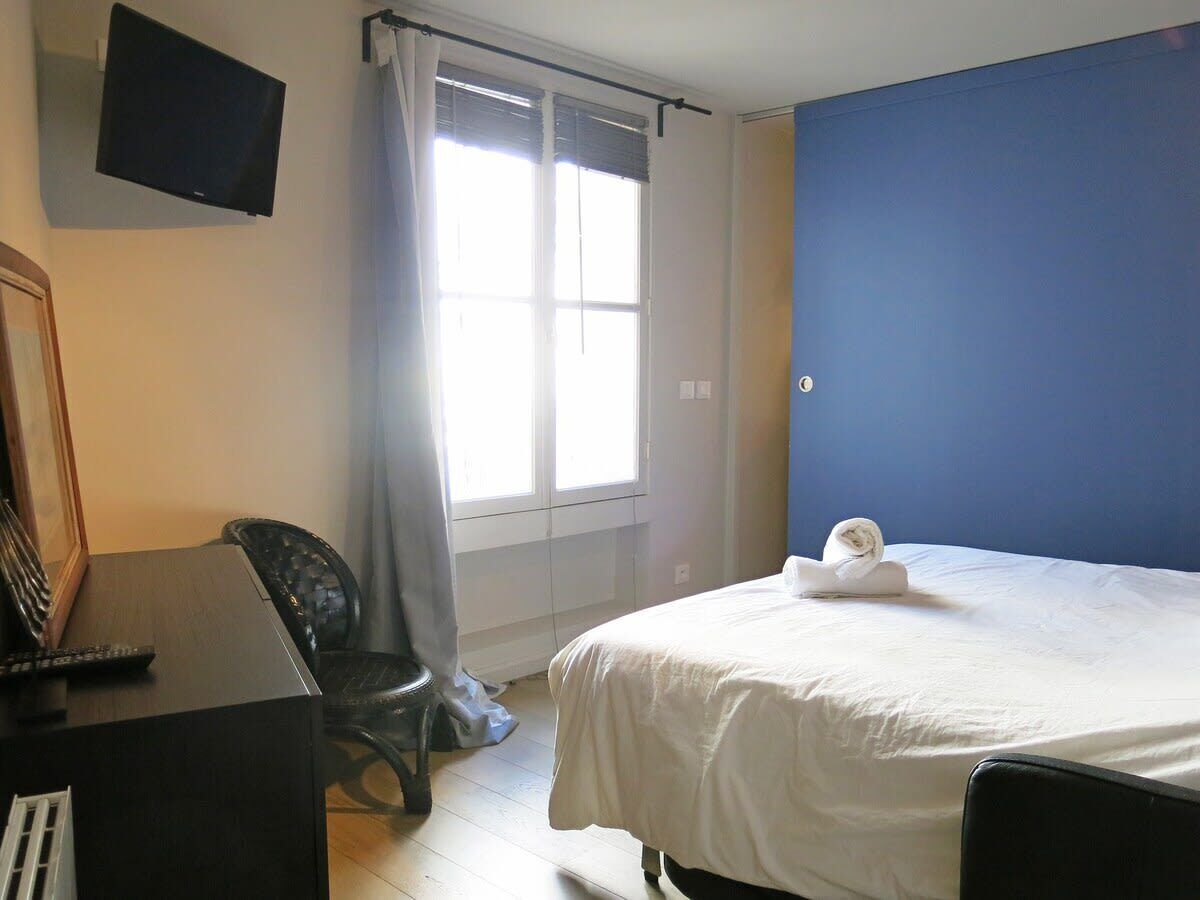Una camera d'albergo con un letto, una scrivania con un computer, una sedia e una TV a parete.