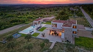 Ein modernes Haus mit Swimmingpool, Sitzgelegenheiten im Freien und Blick auf die umliegende Landschaft.