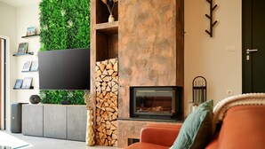 Ein modernes Wohnzimmer mit Kamin, flachbildfernseher an der Wand und einer gemütlichen Sitzecke mit Sofa.