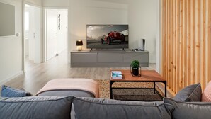 Ein modernes Wohnzimmer mit einem grauen Sofa, einem Holztisch und einem Fernseher auf einem grauen Schrank.
