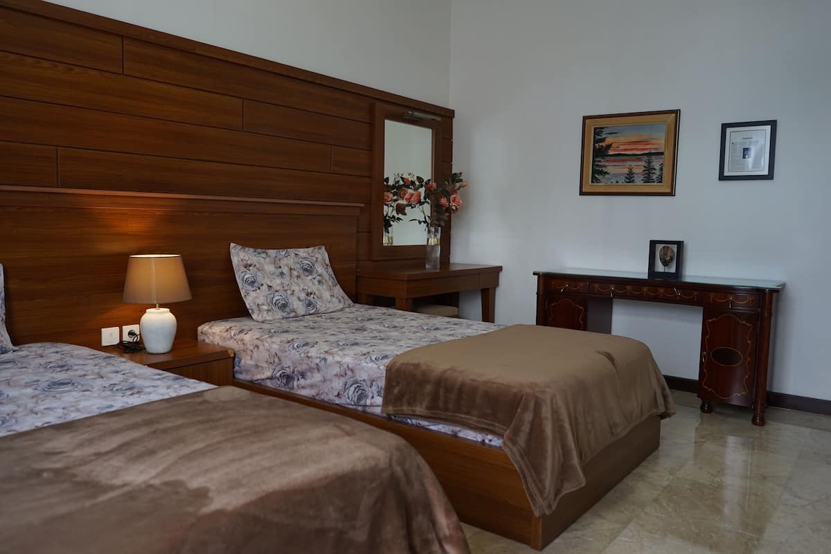 A hotel room with two beds, a wooden headboard, a desk with a mirror, and a framed picture on the wall.