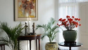 Una habitación bien iluminada con piso pulido, una mesa redonda con un florero de flores rojas y dos plantas en macetas.