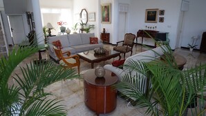 Amplia sala de estar con un conjunto de sofá, una mesa de centro y una mesa auxiliar. Hay plantas en macetas y obras de arte en las paredes.