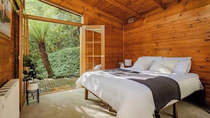 A wooden cabin bedroom with a large bed, a window, and a view of greenery outside. - Seednest Treehouse | Forest & Mountain View (Sassafras)