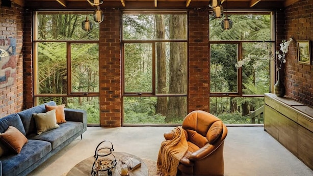 A room with large windows, a blue sofa, a brown leather chair, and a wooden ceiling. - Seednest Treehouse | Forest & Mountain View (Sassafras)