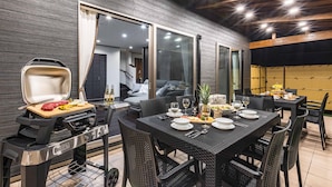 An outdoor dining area with a grill, dining table, chairs, and a view of the interior.