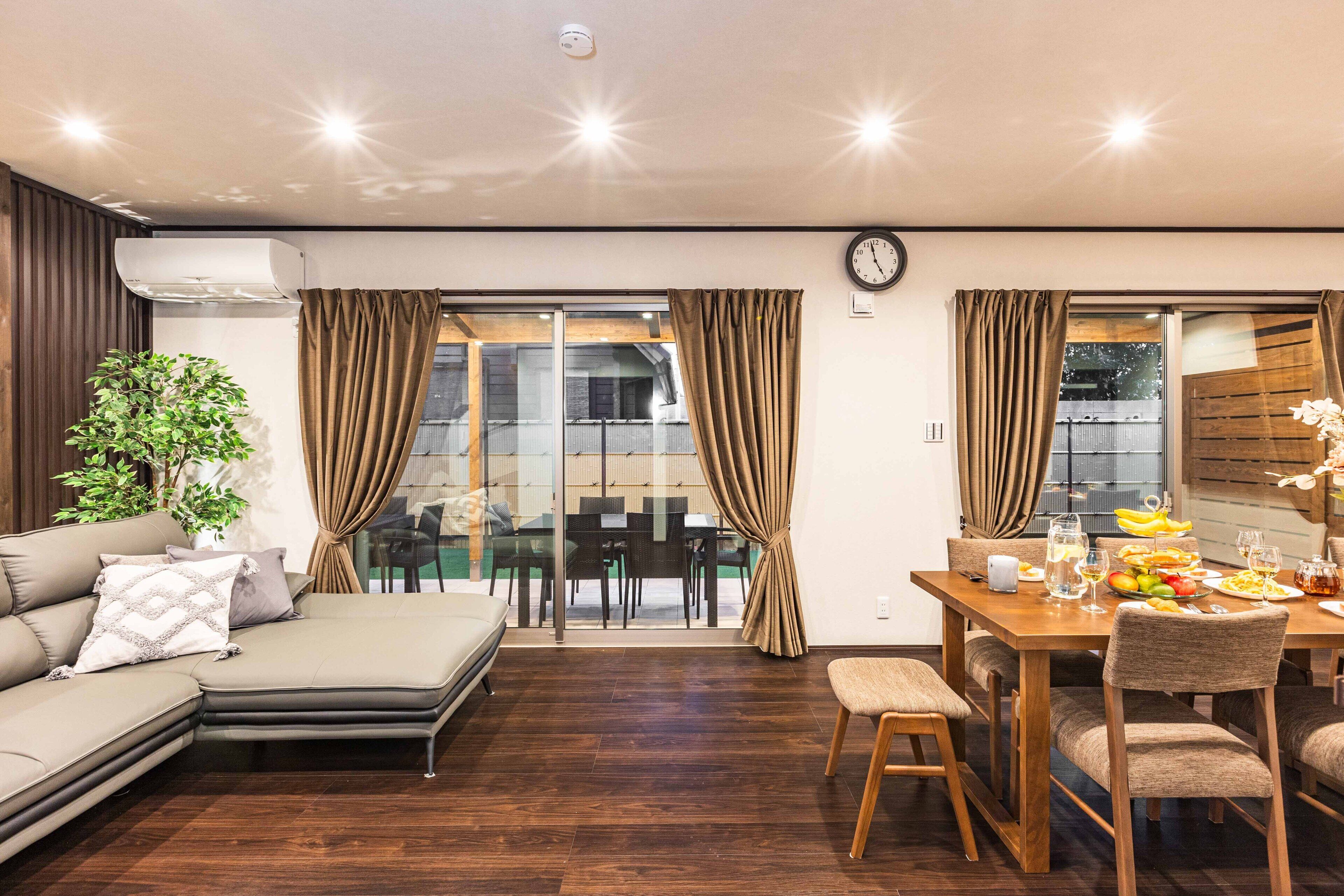 A modern living room with a sofa, dining table, and chairs. There is a potted plant and a clock on the wall.