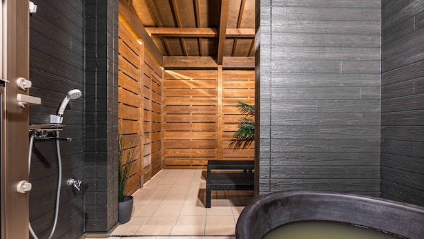 A modern bathroom with a wooden wall, a black bathtub, and a shower area.