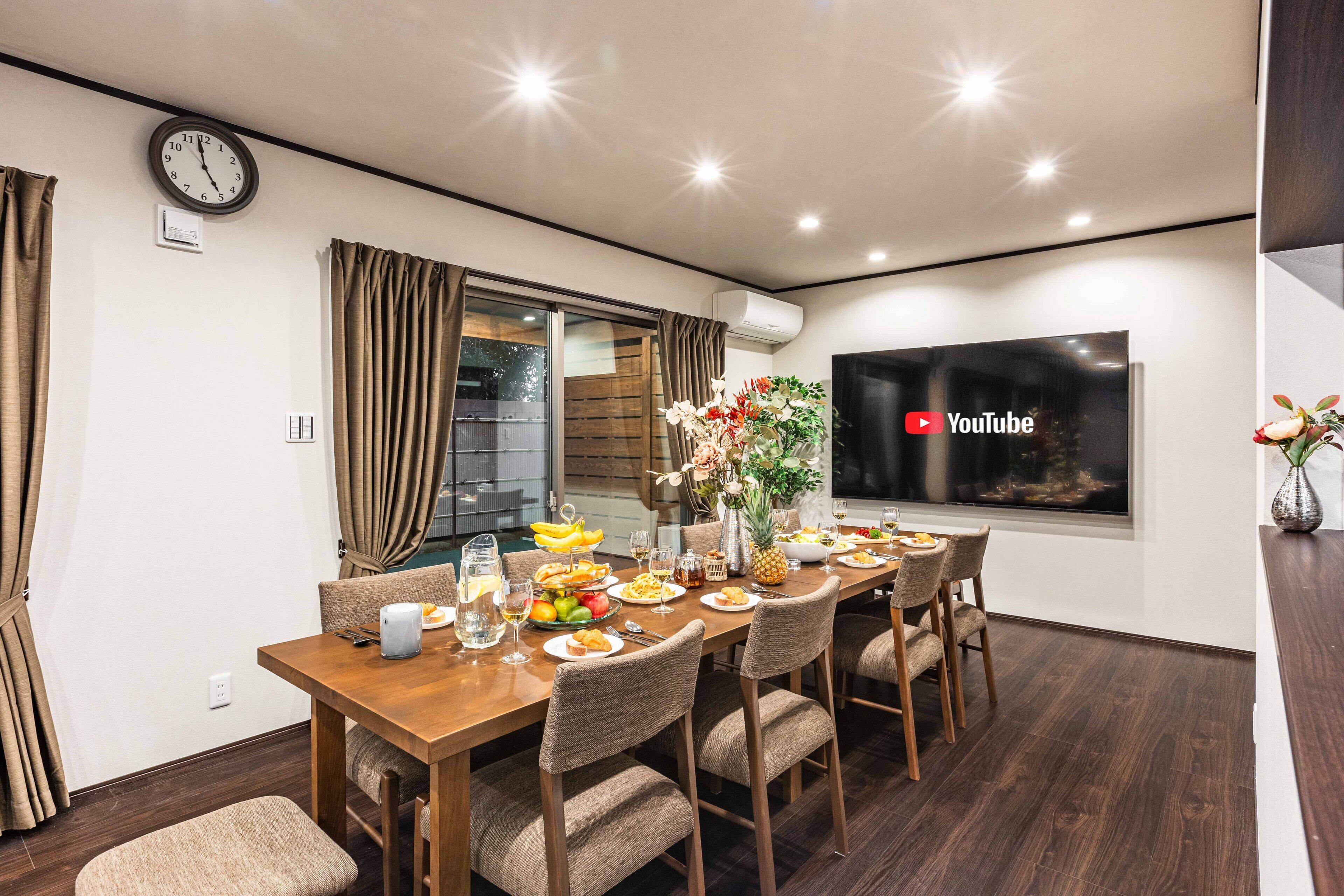A modern dining area with a wooden table set for a meal, a clock, and a YouTube logo on the wall.