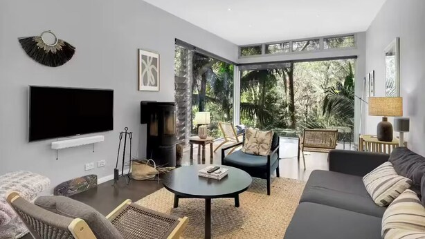 A modern living room with a flat-screen TV, a fireplace, comfortable seating, and large windows offering a view of the outdoors.