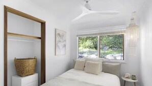 Une chambre à coucher avec un lit, une fenêtre donnant sur un paysage verdoyant, un ventilateur de plafond et un lustre.