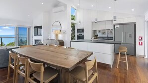Una cocina moderna con armarios blancos, una mesa de comedor de madera y vistas al mar.