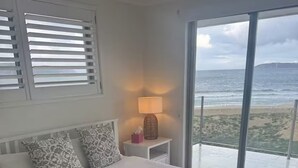 A bedroom with a large bed, a bedside table with a lamp, and a view of the beach. - Luxury Villas Ocean View on the Esplanade (Walk to the beach) (Central Coast)