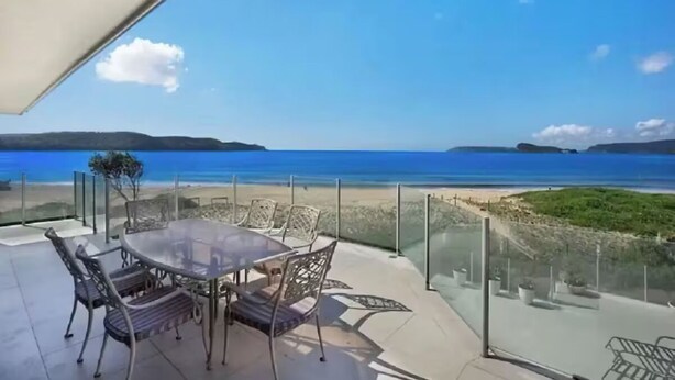 A glass-enclosed outdoor dining area with a table and chairs, overlooking a beach and the sea. - Luxury Villas Ocean View on the Esplanade (Walk to the beach) (Central Coast)