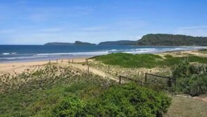 A beach with a path leading to the water, a fence, and a hill in the distance. - Luxury Villas Ocean View on the Esplanade (Walk to the beach) (Central Coast)