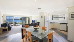 A modern kitchen with a glass dining table, a sofa, and a view of the sea. - Luxury Villas Ocean View on the Esplanade (Walk to the beach) (Central Coast)