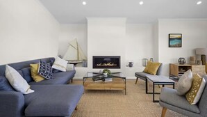 A modern living room with a sofa, armchair, coffee table, fireplace, and artwork on the wall. - Luxury Villas Araluen Waterfront Getaway (Walk to the beach) (Central Coast)