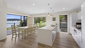 A modern kitchen with a large island, ample natural light, and a view of a body of water. - Luxury Villas Araluen Waterfront Getaway (Walk to the beach) (Central Coast)